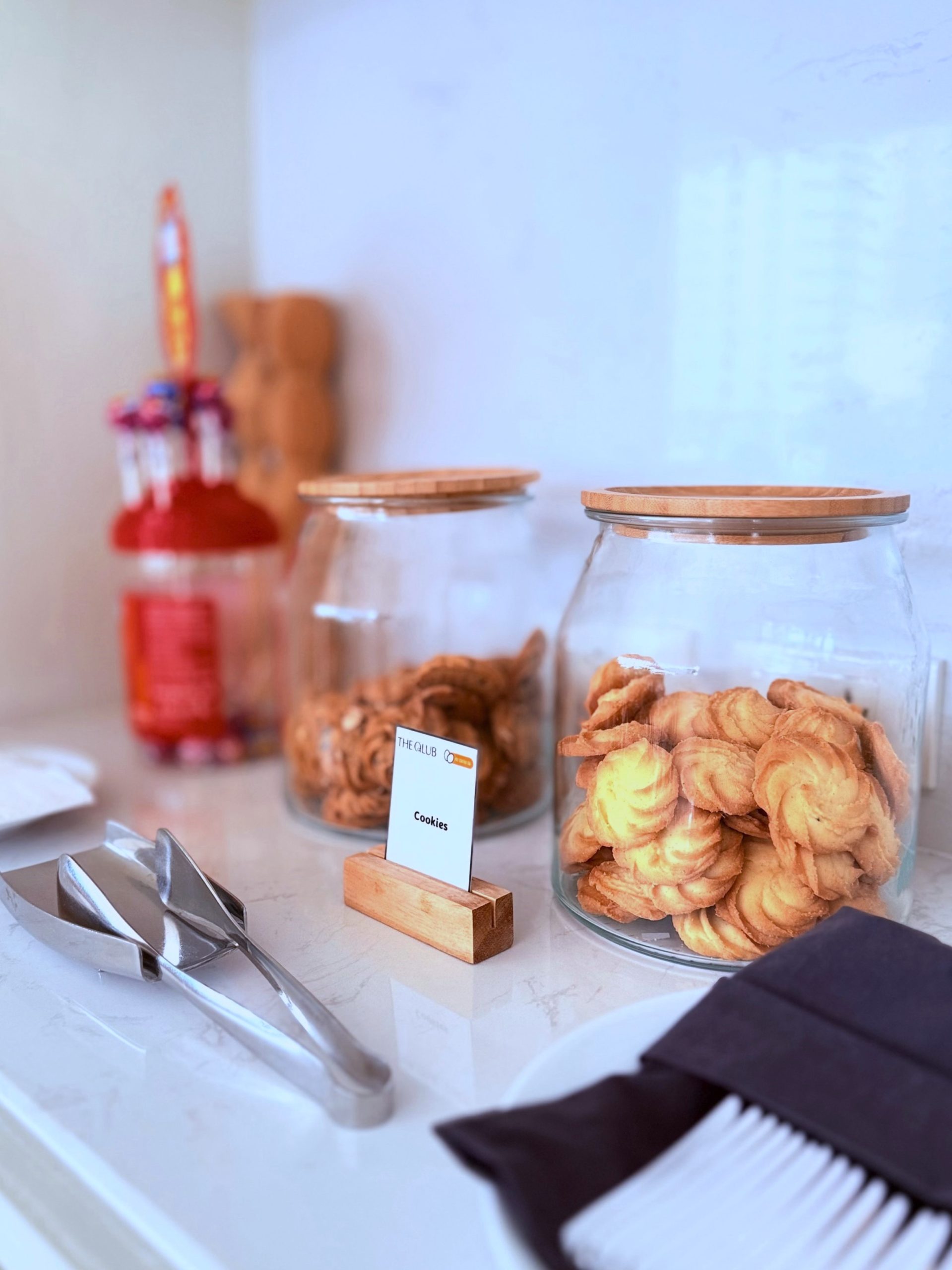 Glass jars filled with buttery cookies at THE QLUB, part of SILQ Hotel’s complimentary afternoon tea for in-house guests. The setup includes serving tongs and napkins, enhancing the high tea experience available daily from 3:00 to 5:00 PM.